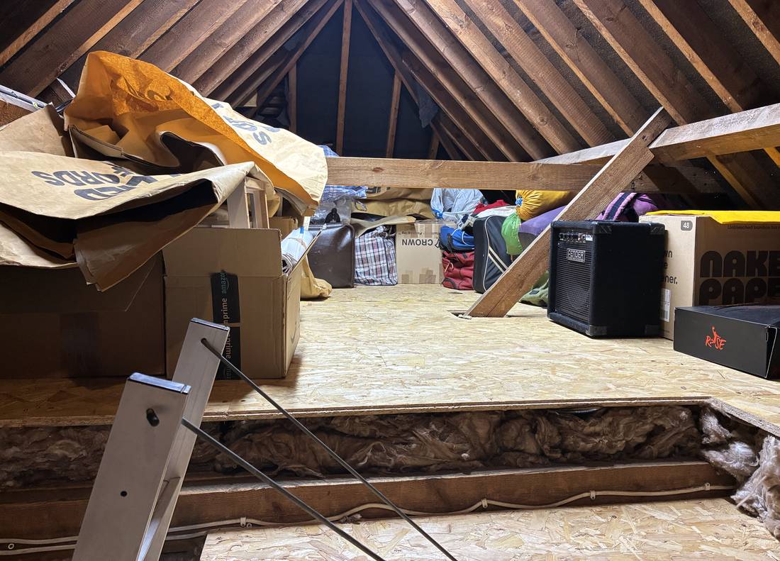 A loft after the work: boxes and cases stored on a raised wooden platform, with the new insulation visible underneath it