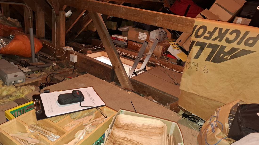 A loft before the work: boxes, bags and loose items covering the floor around the loft hatch